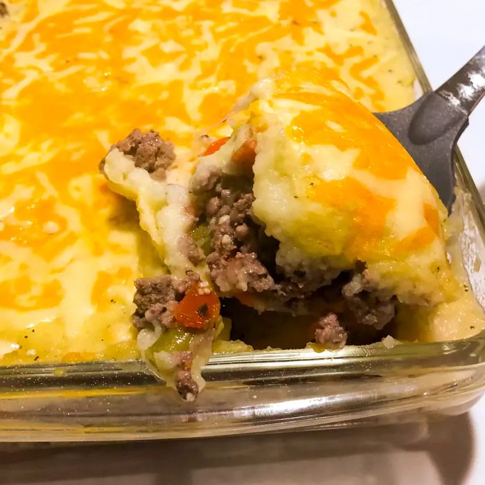 A close-up of Ground Beef Shepherd's Pie in a glass dish, with a serving spoon placed beside it.