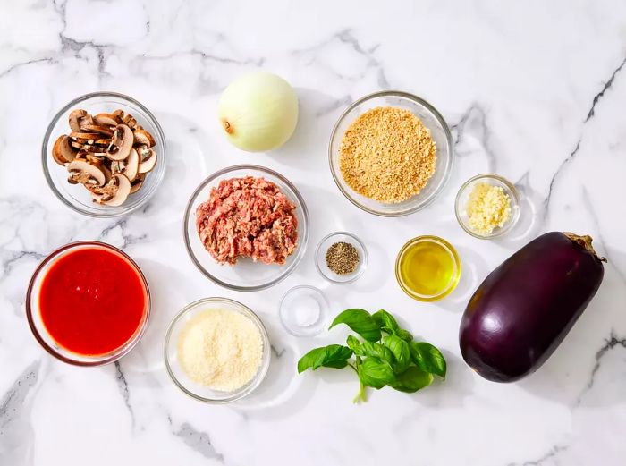 A top-down shot of all the ingredients needed to prepare stuffed eggplant, neatly arranged on a marble countertop.