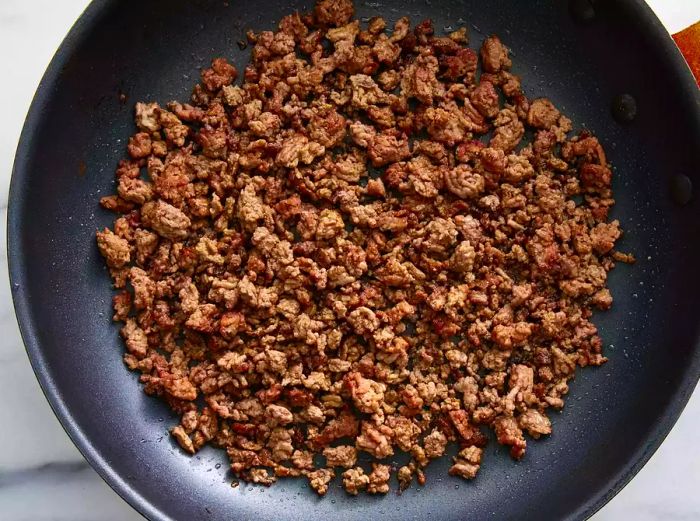 Top view of a skillet with browned ground meat, cooking for stuffed peppers.