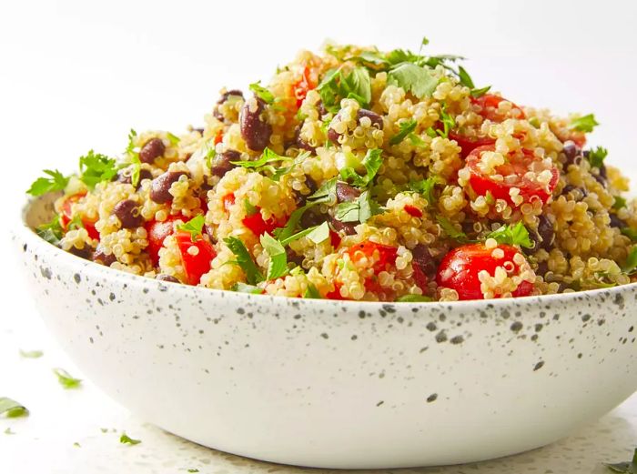 A mid-angle shot of a generous bowl of quinoa salad topped with tomatoes, olives, and fresh herbs.