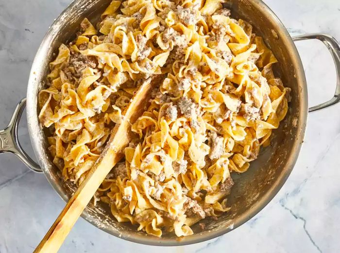 An overhead shot of beef stroganoff being stirred in a pan.