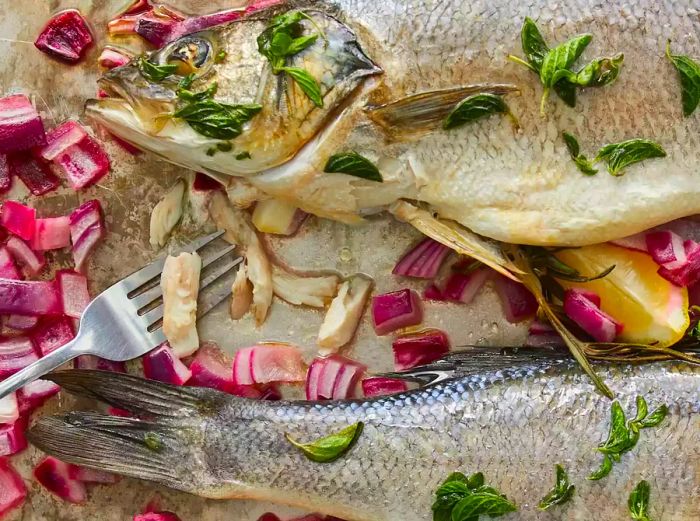 An overhead shot of whole flaky branzino served with a fork, red onions, and lemon.