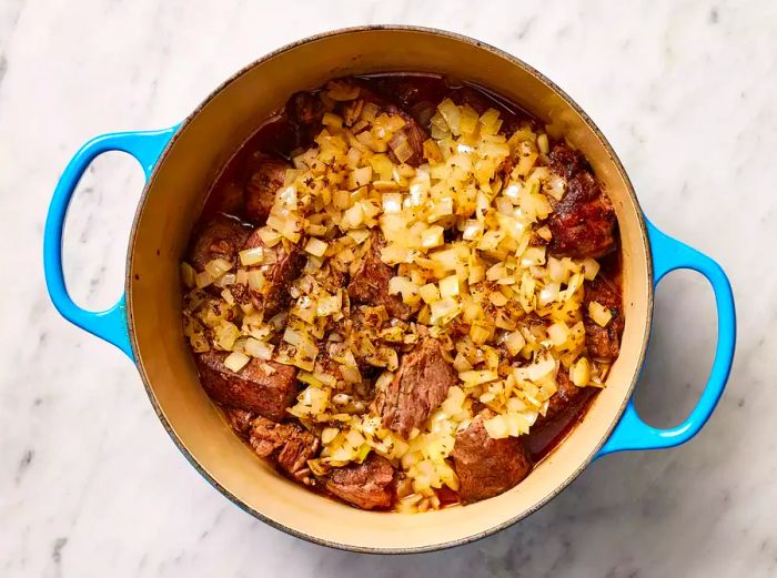 The seasoned broth mixture is added to the stockpot with beef and onions.