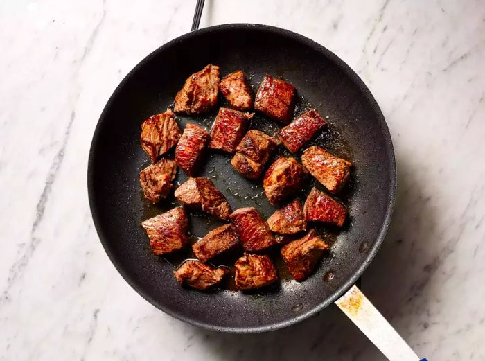 Beef browning in a skillet, getting crispy on all sides.