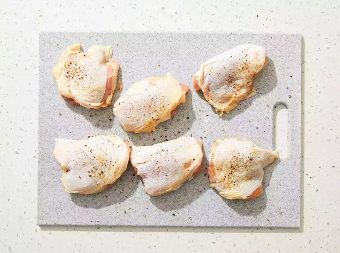 An overhead view of chicken thighs seasoned with salt and pepper resting on a cutting board