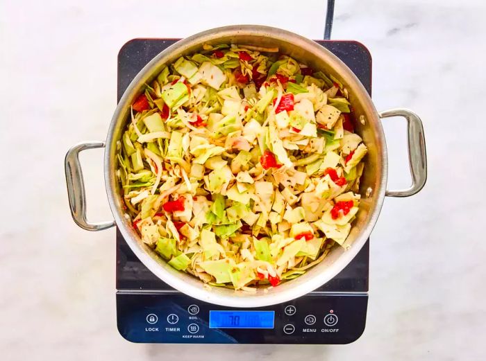 A large pot with cabbage, tomatoes (including juice), onion, Italian seasoning, salt, and pepper.