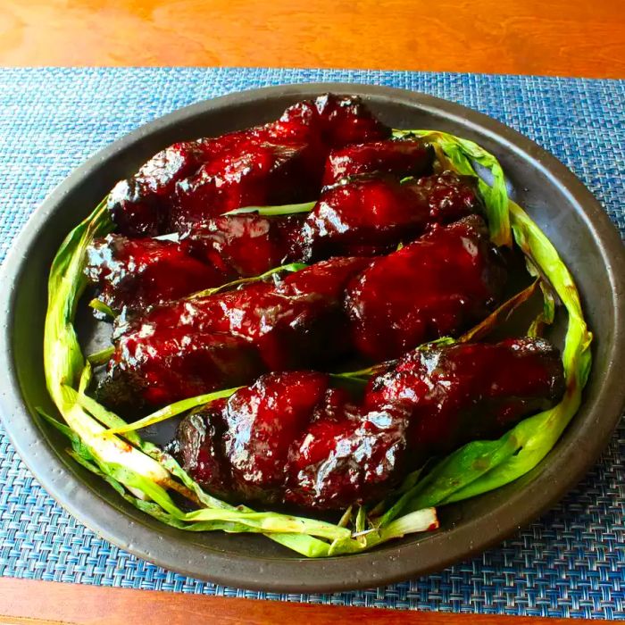 A close-up shot of succulent Chinese Barbeque Pork (Char Siu) paired with fresh green onions, resting in a baking dish.