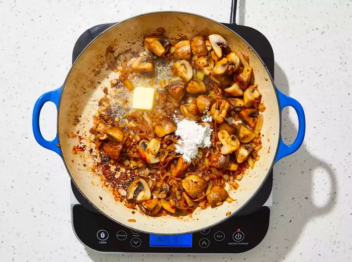 A top-down shot of butter and flour added to a pan of mushrooms, onions, and shallots.