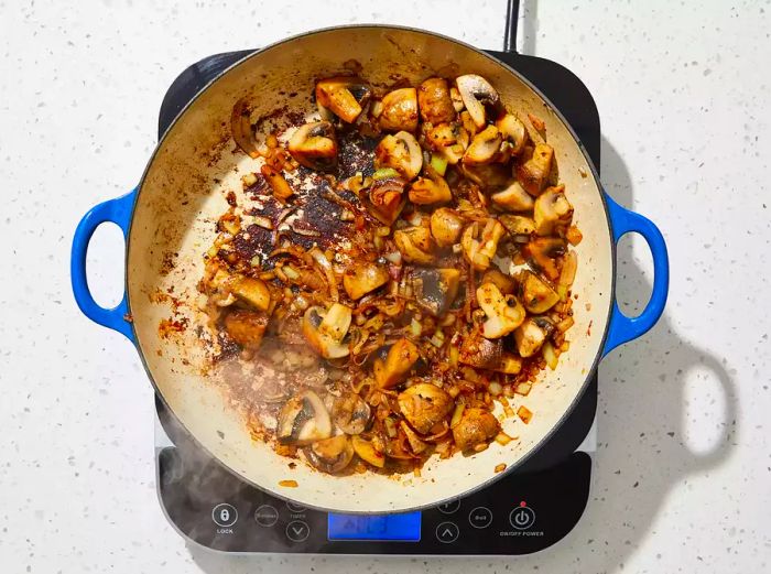 An overhead shot of mushrooms, onions, and shallots sizzling in a skillet.