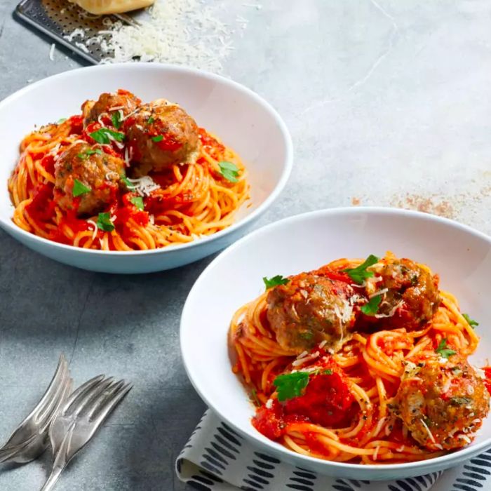 Image of Mozzarella-Stuffed Pesto Turkey Meatballs served over spaghetti in white bowls, topped with grated cheese and fresh basil leaves.