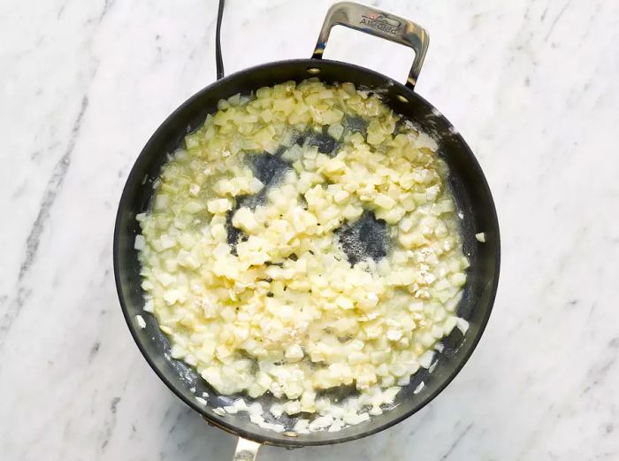 A top-down shot of onions sautéing in butter, mixed with garlic powder and flour in a skillet