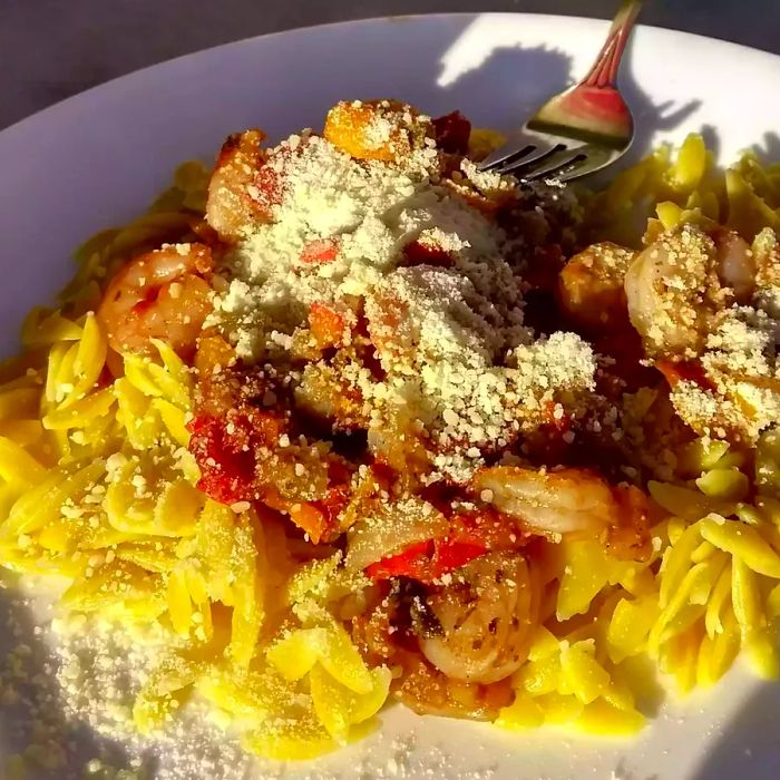 A close-up of Shrimp Orzo Pesto plated and garnished with cheese, accompanied by a fork.