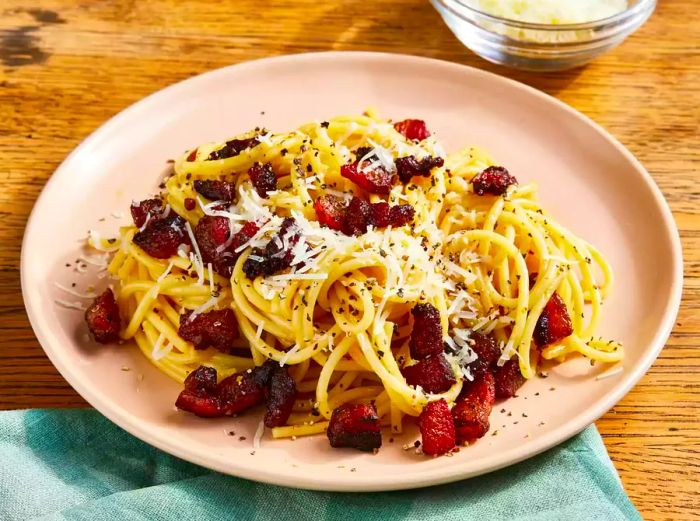 High-angle view of a plate filled with spaghetti alla carbonara, garnished with a generous topping of cheese