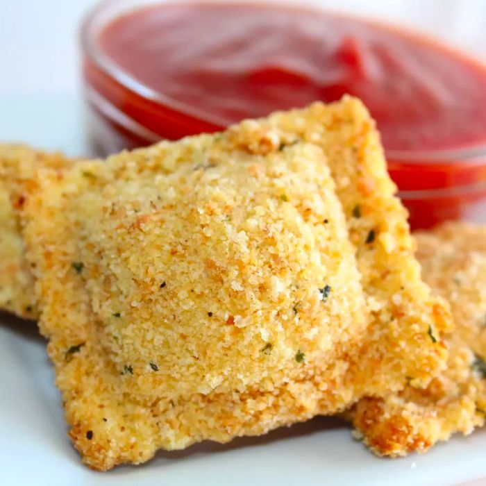 Close-up shot of crispy breaded ravioli served with marinara sauce in a glass bowl.