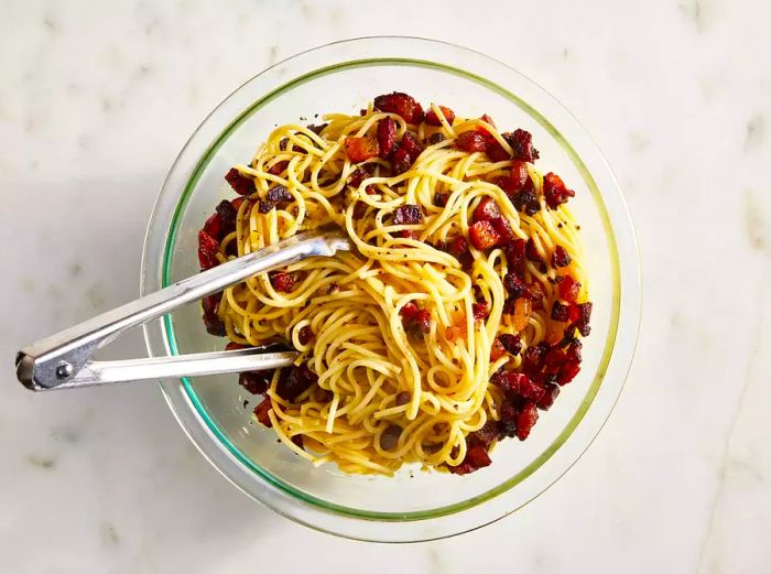 Overhead shot of carbonara pasta in a bowl with tongs