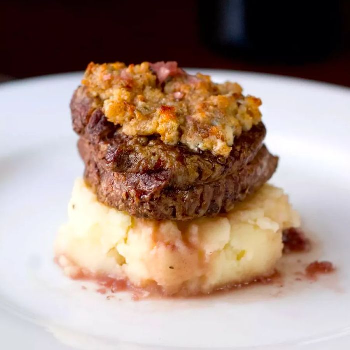 Close-up shot of Blue Cheese Crusted Filet Mignon with Port Wine Sauce, resting atop creamy mashed potatoes on a white plate.