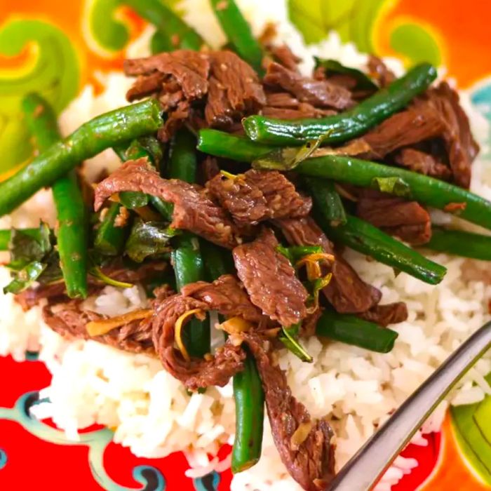 A close-up shot of Thai-style beef with green beans served over white rice on a vibrant plate.