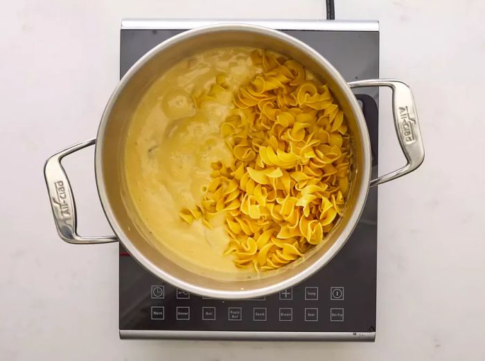 A pot on the stove with chicken, condensed soup, and pasta cooking together.