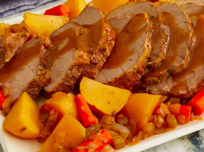 Side view close-up of sliced eye of round roast served with vegetables on a platter