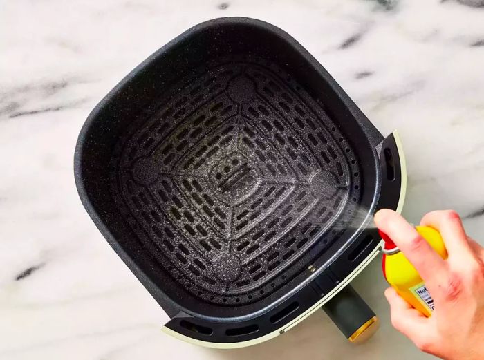 The inside of the air fryer basket is sprayed with cooking spray.