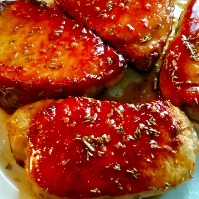 A close-up view of center-cut pork chops glazed with a rich, amber-hued sauce, topped with dried herbs for a finished look.