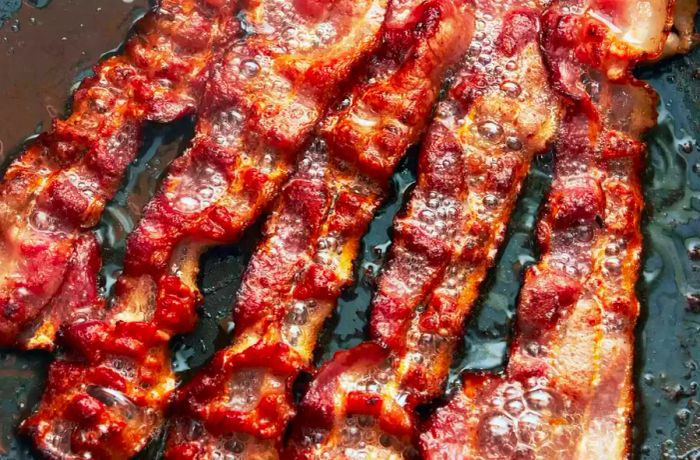 A slice of bacon sizzling in a frying pan.