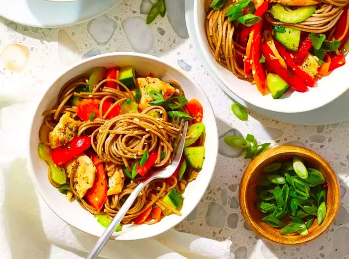 An overhead shot showing a bowl of soba noodle salad topped with chicken and sesame seeds.