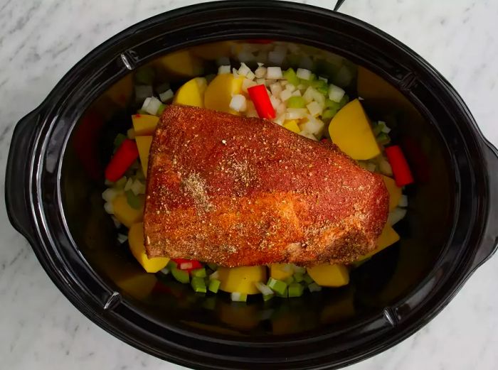 Overhead view of an eye of round roast resting atop vegetables inside a slow cooker