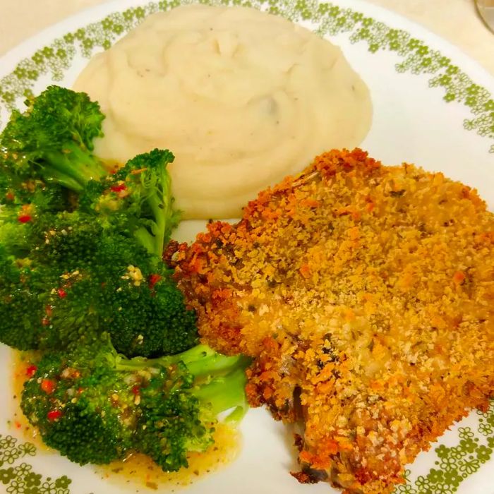 A close-up shot of a delicious pork chop served alongside mashed potatoes and broccoli.