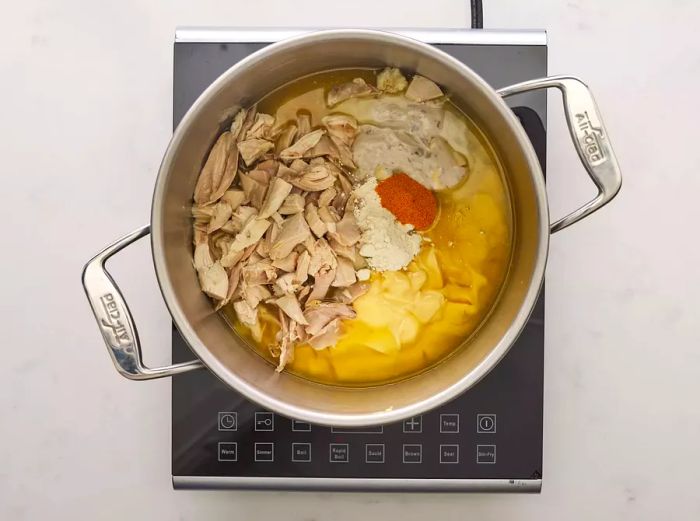 A pot on a burner containing chicken, condensed soup, onion powder, seasoning salt, and garlic powder.