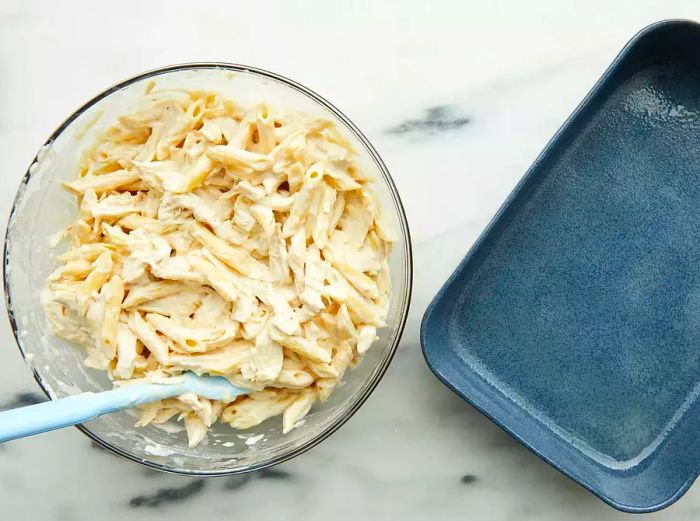 Aerial view of the chicken Alfredo casserole ingredients mixed together in a bowl, with a baking dish placed to the side.