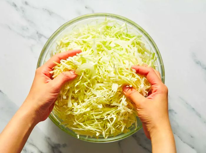 Hands mixing shredded cabbage strips for salad prep.