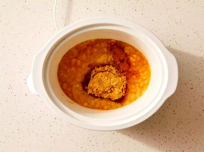 A slow cooker with chunky applesauce, enhanced with brown sugar and pumpkin pie spice