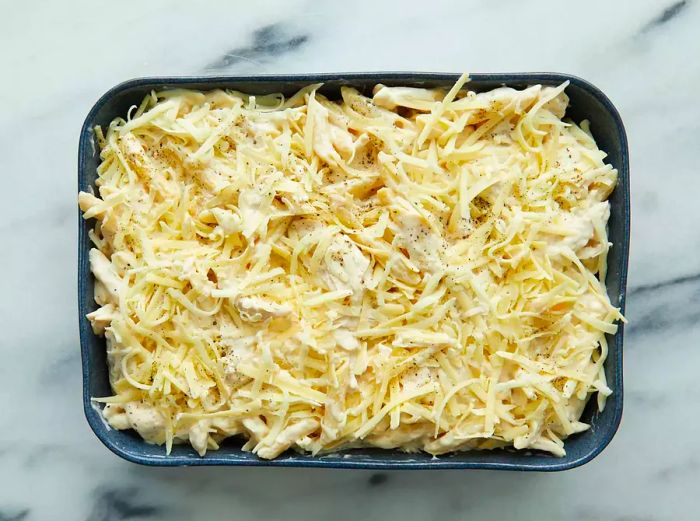 Aerial view of an uncooked chicken Alfredo casserole in a baking dish, generously covered with cheese.