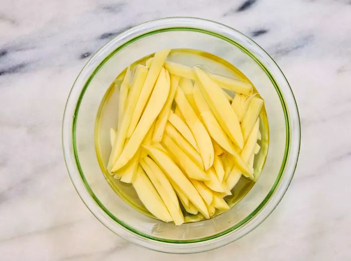 A clear bowl filled with sliced potatoes soaking in the water