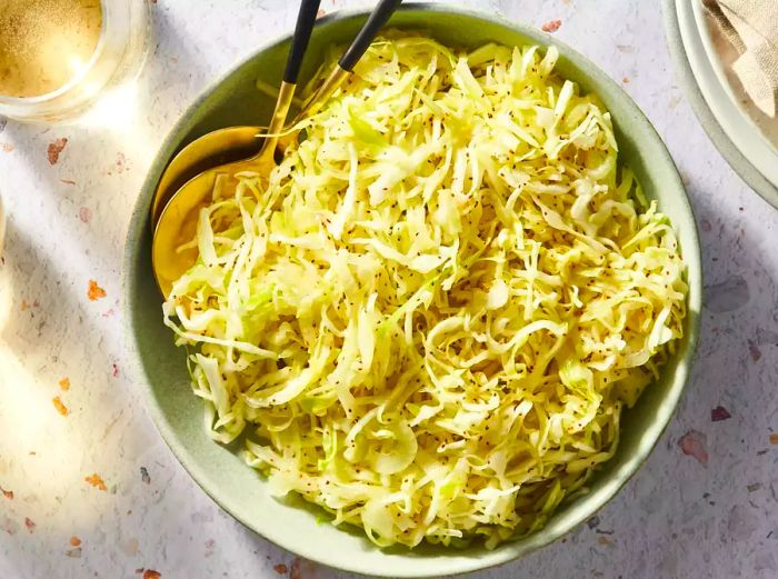 A bowl of freshly shredded Amish slaw placed on a speckled surface.