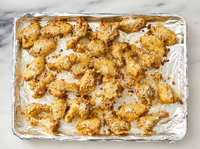 Uncooked chicken wings arranged on a baking sheet lined with foil