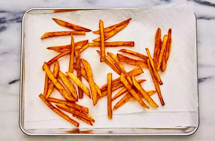 A baking sheet lined with paper towels, holding French fries