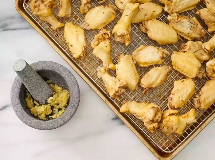 Golden cooked chicken wings on a metal rack placed over a baking sheet, with a mortar and pestle beside it, filled with seasonings