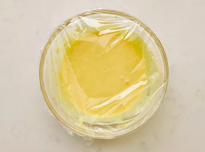 A glass bowl of honey mustard dipping sauce wrapped in plastic film.