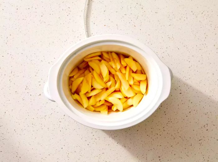 A slow cooker filled with sliced apples and water