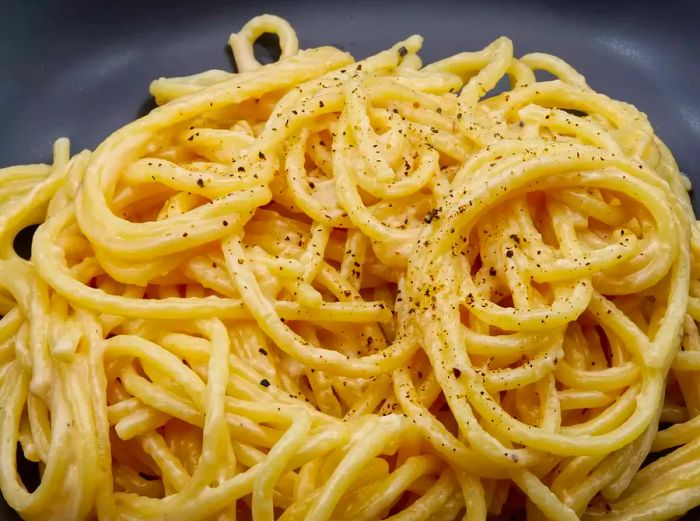 A plate of spaghetti cacio e pepe served on a black dish