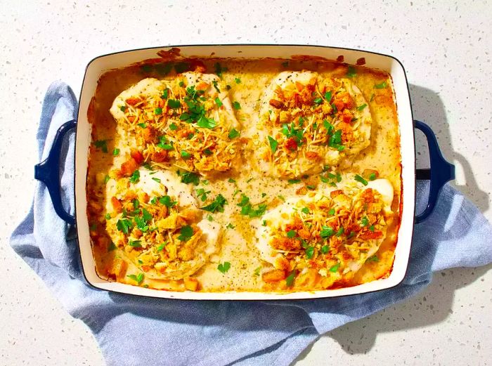 A top-down view of a 9x13 baking dish with four baked Caesar chicken breasts, garnished with fresh parsley.