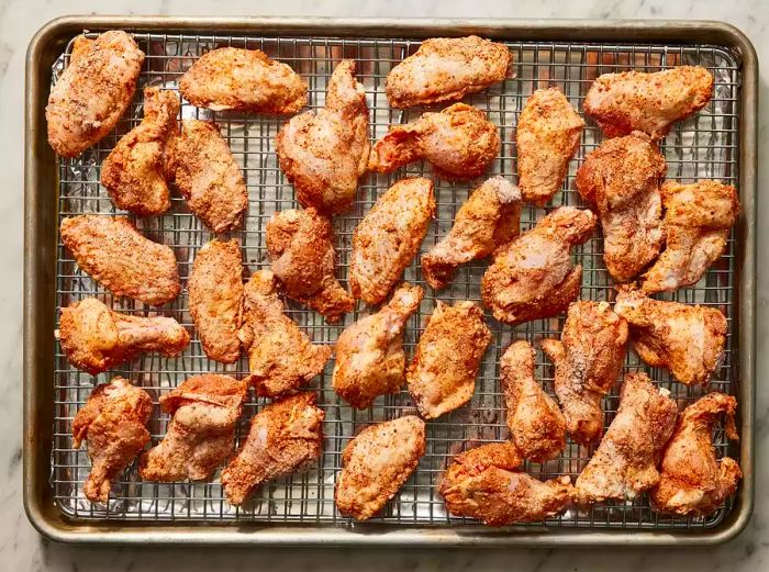 Chicken wings coated in seasoning arranged neatly on a wire rack placed over a baking sheet.