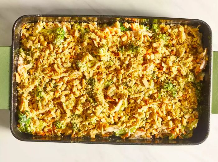 A layer of breadcrumbs scattered over the chicken casserole in a baking dish, ready for the oven.