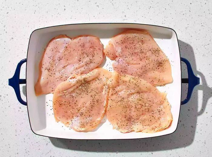 Chicken seasoned with salt and pepper, then arranged in the baking dish.