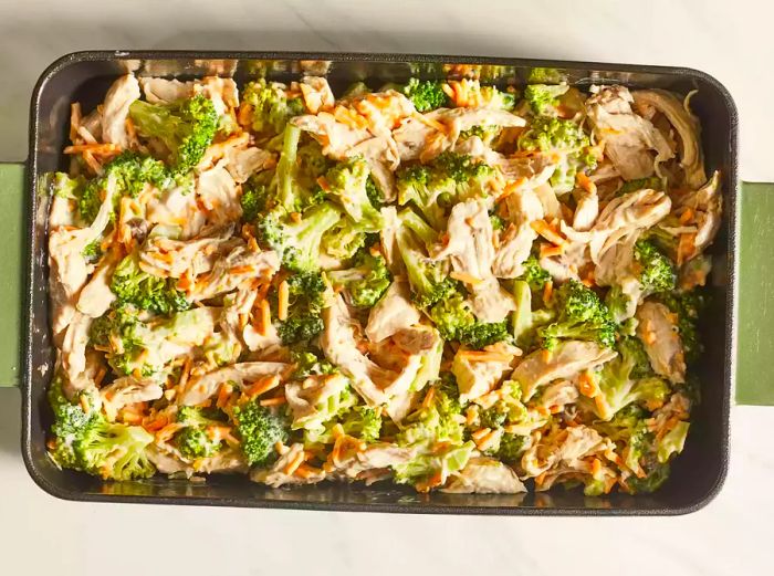 An overhead view of chicken, broccoli, and cheese layered in a baking dish, ready to be baked.