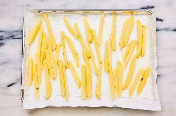 A baking sheet lined with paper towels, holding sliced potatoes