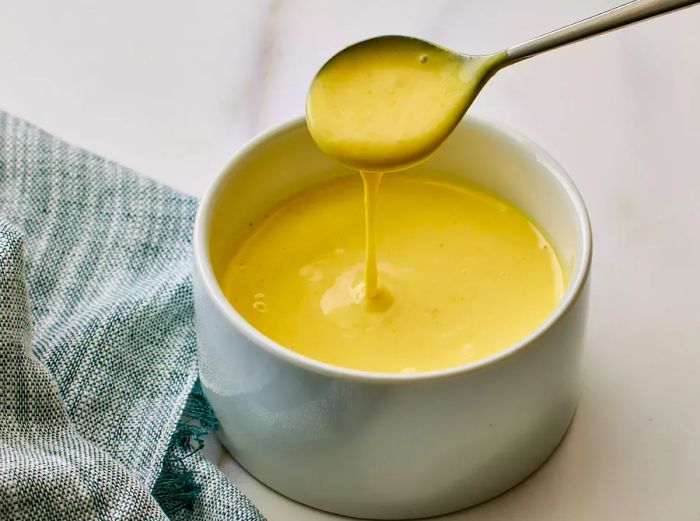 A small bowl of honey mustard dipping sauce, with a spoon dripping sauce into it.