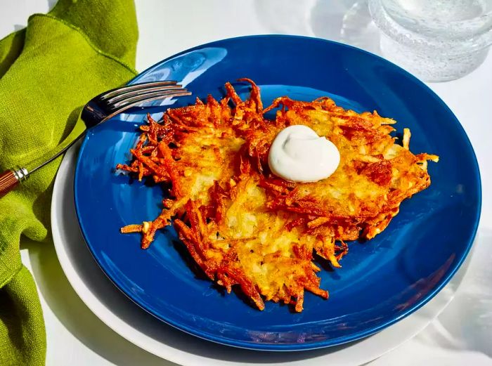 A plate of three golden, crispy German potato pancakes, each topped with a spoonful of sour cream